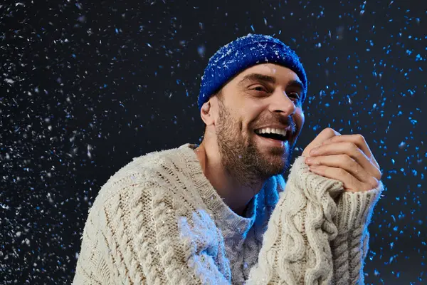 A young man smiles broadly while surrounded by falling snowflakes, radiating warmth and happiness. — Stock Photo
