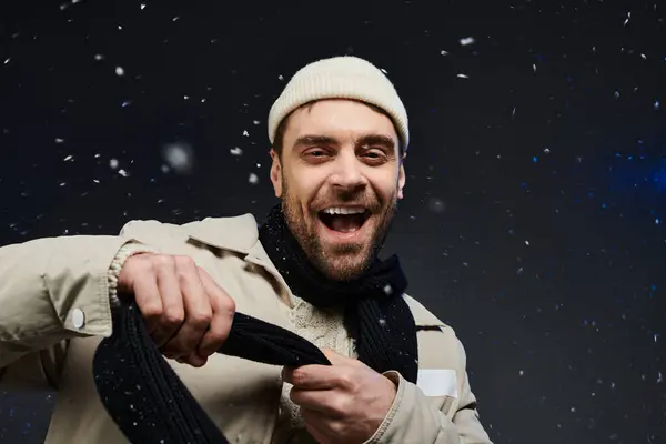The young man beams with joy, wrapped in a cozy scarf amidst falling snowflakes. — Stock Photo