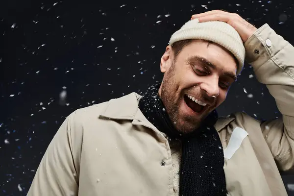 A handsome young man smiles widely while snowflakes fall gently around him during winter. — Stock Photo