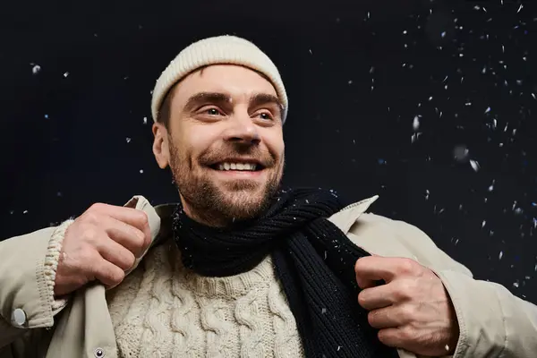 Un joven sonriente abraza el frío invernal con felicidad, vistiendo un suéter cálido y una bufanda. - foto de stock