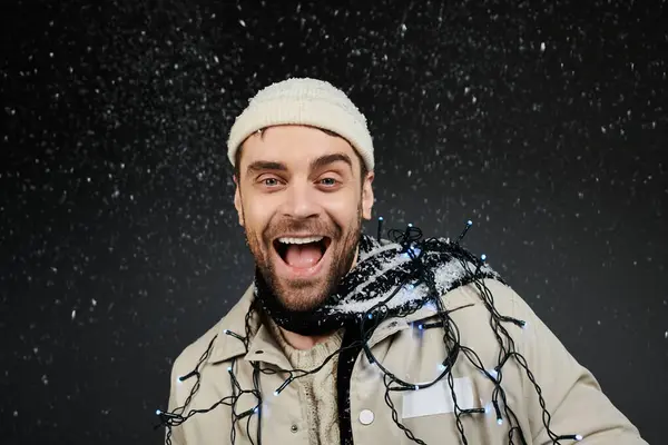 A smiling young man with a knit hat enjoys the winter ambiance with snowflakes and lights. — Stock Photo