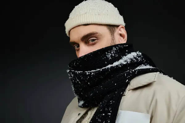 Un bel giovane vestito calorosamente si erge con un'espressione pensierosa mentre cadono i fiocchi di neve. — Foto stock