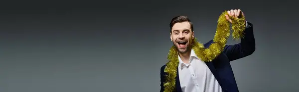 A joyful young man wearing a suit plays with shimmering gold tinsel, embracing a festive mood. — Stock Photo