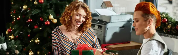 Two coworkers share laughter and gifts surrounded by festive office decorations during Christmas. — Stock Photo