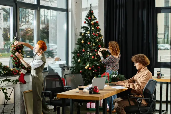 I colleghi adornano allegramente un albero di Natale e uno spazio di lavoro con decorazioni festive. — Stock Photo