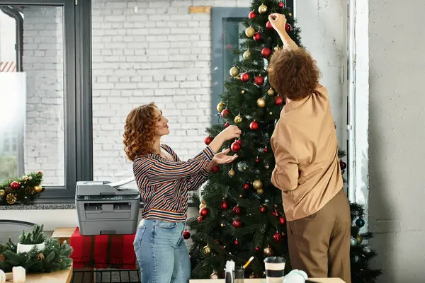 Due giovani colleghi stanno allegri aggiungendo ornamenti ad un albero di Natale in ufficio. — Foto stock