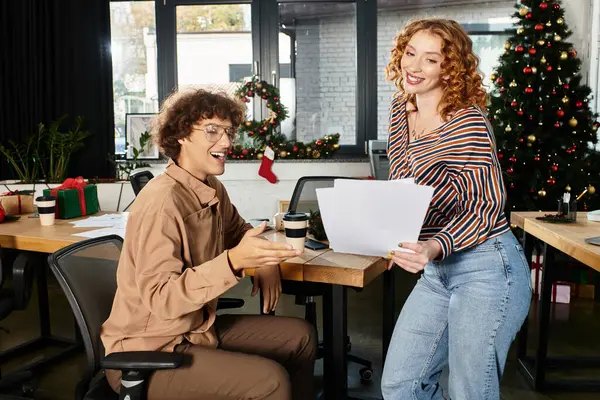 Dois jovens colegas de trabalho se envolvem em alegria festiva enquanto celebram o Natal no trabalho. — Fotografia de Stock