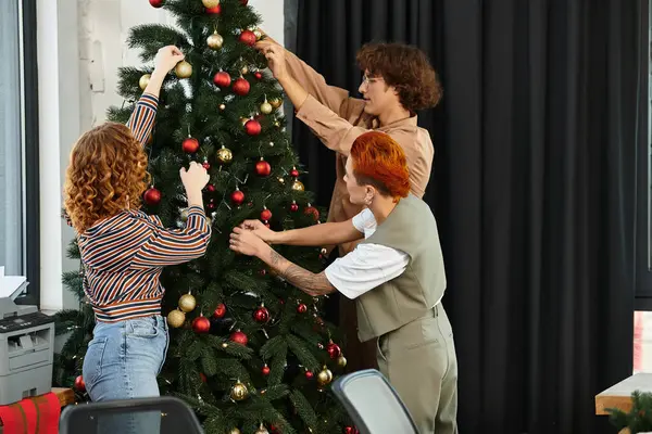 A group of colleagues collaborates to beautifully adorn a Christmas tree in their workspace. — Stock Photo