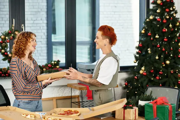Two coworkers share a warm moment, exchanging gifts amidst holiday decorations in the office. — Stock Photo