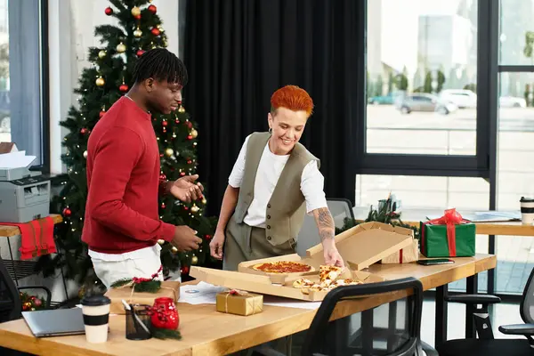 Zwei fröhliche Mitarbeiter genießen Pizza und Lachen, während sie die Weihnachtszeit in ihrem Büro feiern. — Stockfoto