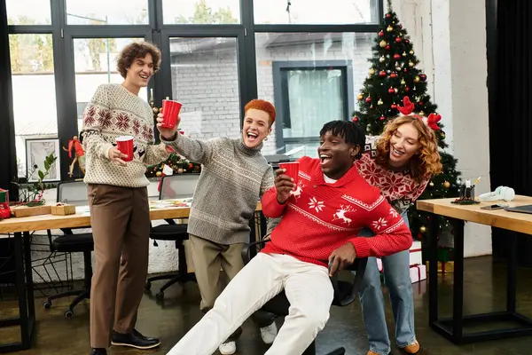 Coworkers in Christmas sweaters cheerfully raise cups while enjoying the holiday spirit at work. — Stock Photo