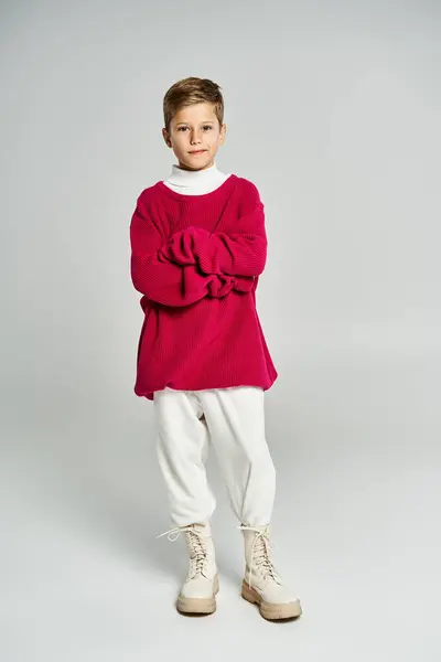 A boy showcases a vibrant red sweater with white pants and boots, exuding winter charm. — Stock Photo