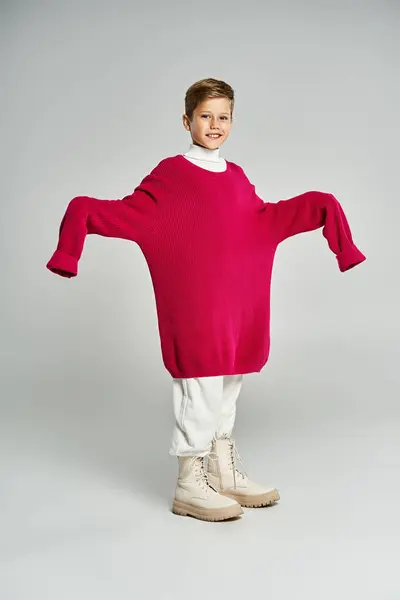 Un ragazzo allegro indossa un grande maglione rosa e sorride, incarnando calore invernale e divertimento.. — Foto stock