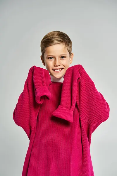 A young boy wears an oversized pink sweater, smiling happily while embracing warmth and comfort. — Stock Photo