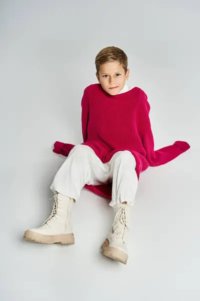 A boy sits comfortably on a soft surface, wrapped in a bright sweater with stylish boots. — Stock Photo