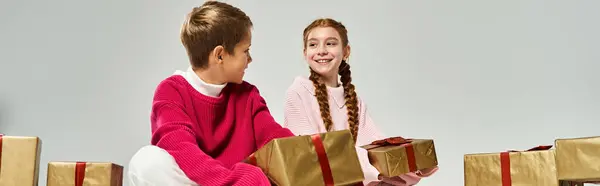 Two joyful children in warm clothing share smiles while playing with holiday gifts. — Stock Photo