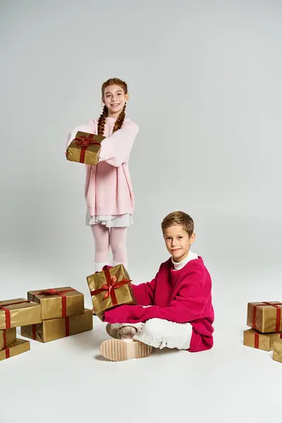 A boy and girl happily explore wrapped presents in cozy winter outfits surrounded by holiday cheer — Stock Photo