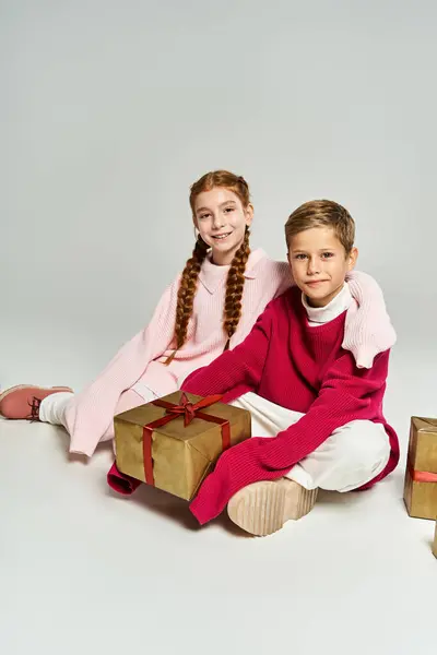 Zwei Kinder in warmer Winterkleidung sitzen fröhlich mit schön verpackten Geschenken beisammen. — Stockfoto