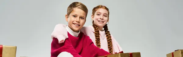 Two happy children dressed warmly share smiles while surrounded by colorful presents in winter. — Foto stock