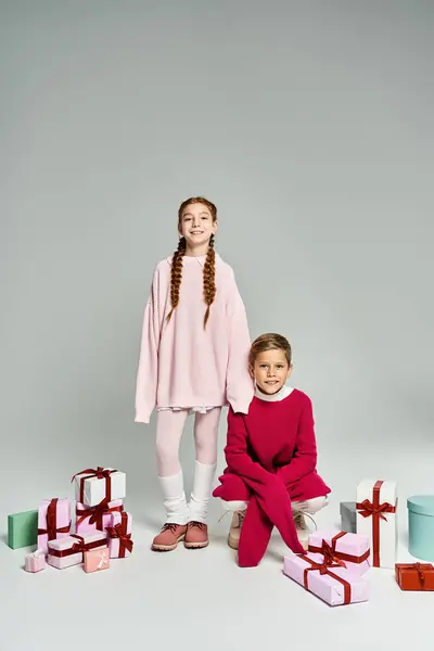 Two cheerful kids in warm attire pose happily among colorful wrapped presents. — Stock Photo