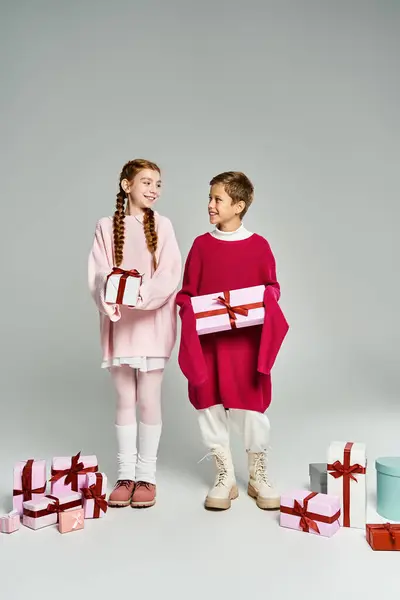 Two children in warm sweaters exchange presents with cheerful expressions during winter festivities. — Stock Photo