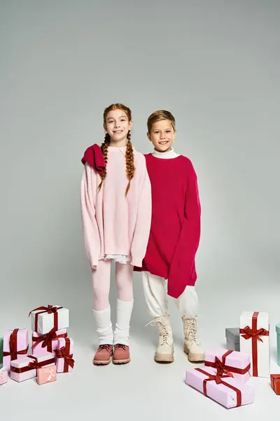 Two kids in cozy winter outfits stand by colorful gift boxes filled with cheer. — Stock Photo