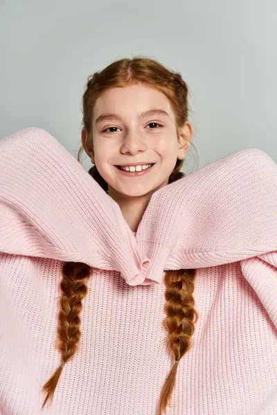 A young girl in a large pink sweater beams with joy while wearing her hair in braids. — Stock Photo