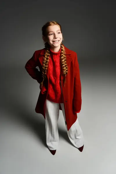 A young girl dressed warmly in a bright red sweater and stylish coat smiles happily indoors. — Stock Photo