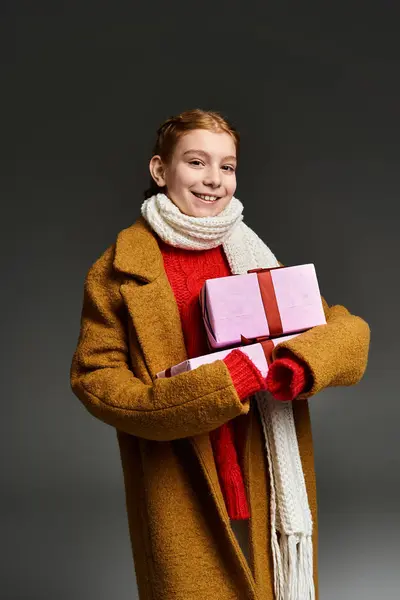 A cheerful young one dons warm winter clothing while cradling festive presents with delight. — Stock Photo