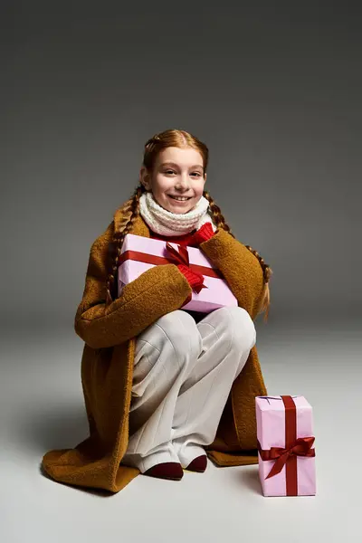 A cheerful young girl in warm clothes embraces beautifully wrapped presents with glee. — Stock Photo