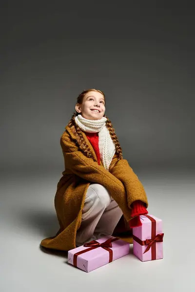 A young girl in warm attire smiles happily while hugging a blanket and surrounded by gifts — Fotografia de Stock