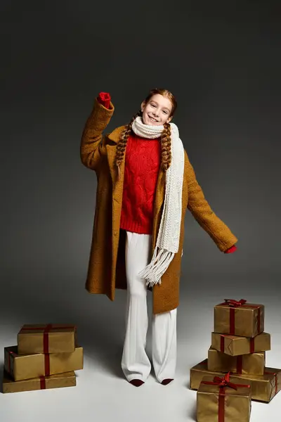 A cheerful girl dressed in warm winter clothes poses joyfully by beautifully wrapped gifts. — Stock Photo