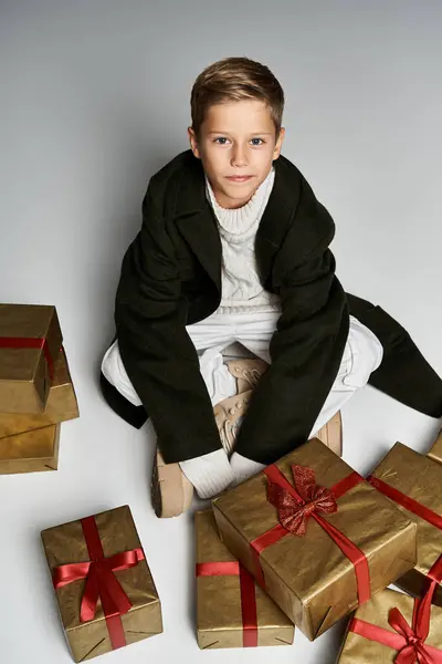 Un jeune garçon habillé chaleureusement profite d'un moment entouré de cadeaux festifs pendant l'hiver. — Photo de stock