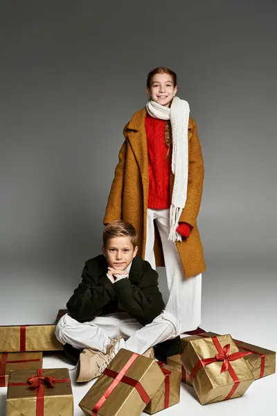 Two children dressed warmly pose playfully with beautifully wrapped gifts during winter. — Stock Photo