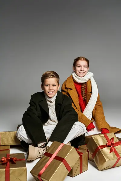Two cheerful kids dressed in warm winter outfits enjoy the festive season with holiday presents. — Stock Photo