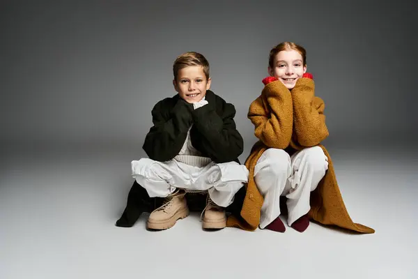 Two children sit happily in cozy winter outfits, radiating warmth and joy during a chilly day. — Stock Photo
