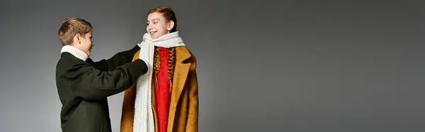 Two siblings joyfully prepare for winter, wrapping up in cozy scarves and winter clothing together. — стоковое фото