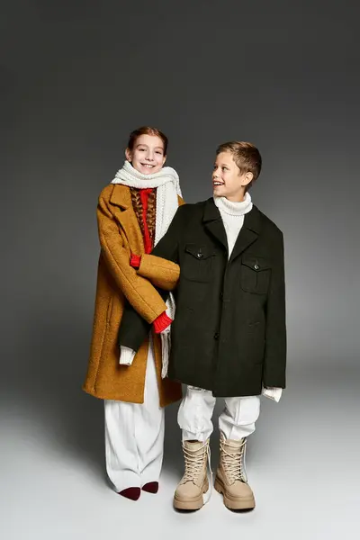 Due bambini felici in cappotti invernali condividono un grande cappotto mentre si abbracciano. — Foto stock