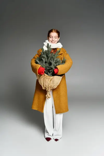 A cheerful girl dressed in cozy winter clothes embraces a small tree with joy. — Stock Photo