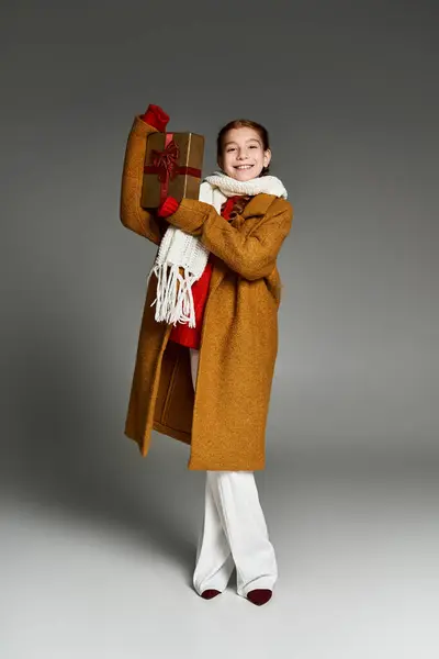 A cheerful girl dressed in warm winter clothes is excitedly presenting a gift. — Stock Photo