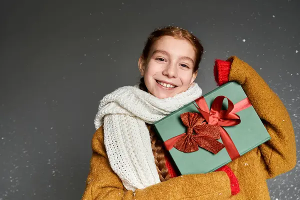 A cheerful girl in warm clothes smiles, holding a colorful present for winter festivities. — Stock Photo