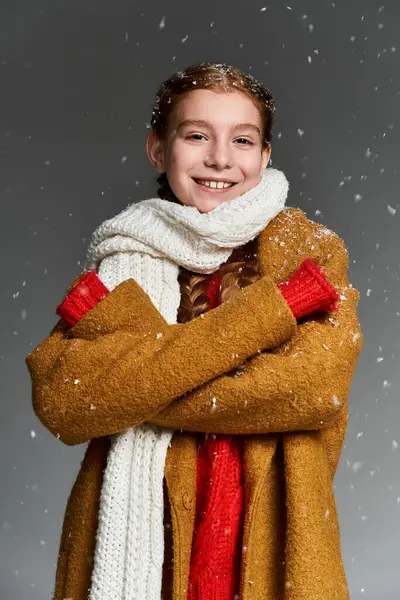 A happy girl stands warmly dressed in winter layering, embracing falling snowflakes. — Stock Photo