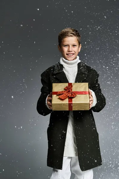 A young boy smiles brightly while showcasing a present amid softly falling snowflakes. — Foto stock