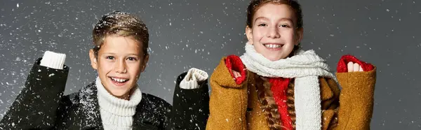 Zwei glückliche Kinder in warmen Kleidern genießen den Schneefall um sie herum. — Stockfoto