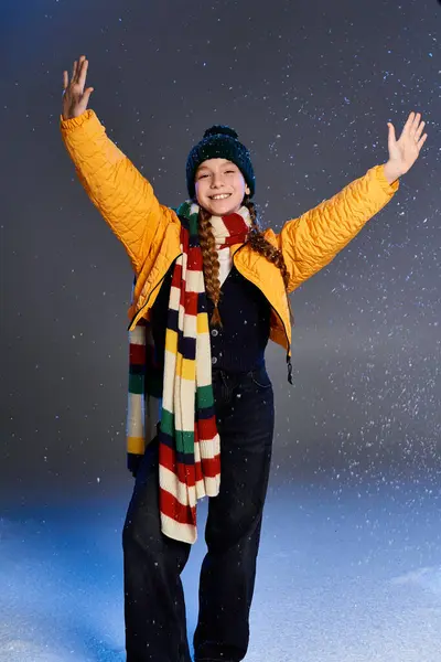 A cheerful girl wearing cozy winter clothing joyfully welcomes the snow with open arms. — Stock Photo