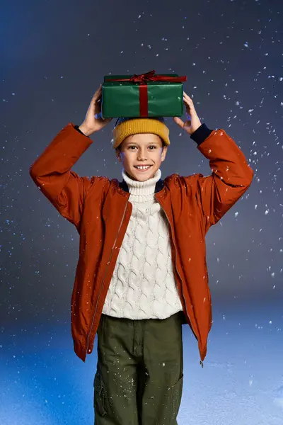A boy in a cozy sweater and orange jacket happily holds a gift above their head in the snow. — Stock Photo