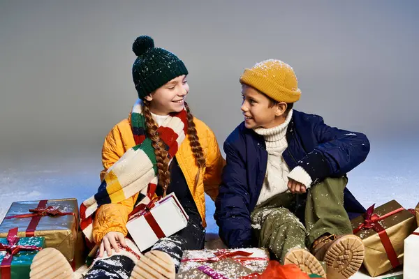 Two young friends dressed in warm winter clothing share joy and presents in a snowy atmosphere. — Stock Photo