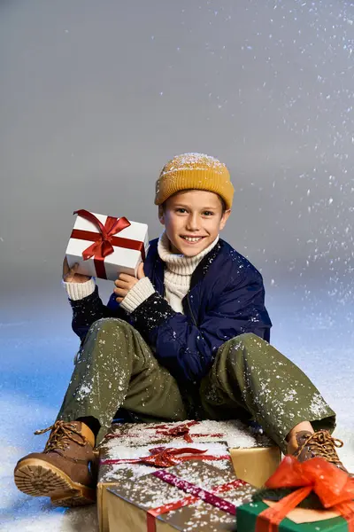 Un niño alegre con ropa de invierno sonríe brillantemente entre las cajas de regalo festivas. - foto de stock