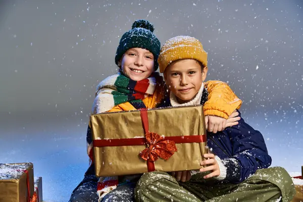 In a cozy winter setting, two happy kids embrace while surrounded by festive gifts. — Stock Photo