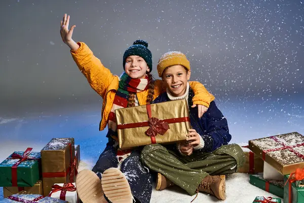 Two happy children enjoy a snowy winter wonderland while surrounded by colorful presents. — Stock Photo
